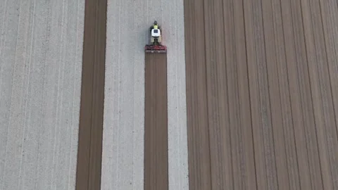 Slow-motion top-down drone shot of tractor leveling striped fields at Maginot Stock Footage 308444257