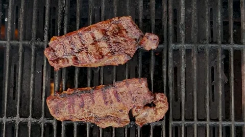 Slow Motion Top View of Two Juicy Sirloin Steaks Grilling on Black BBQ Grill Stock Footage 339217613