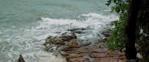Slow-motion top view of water crashing on a shore with rocks on a cloudy day Video stock 127372417