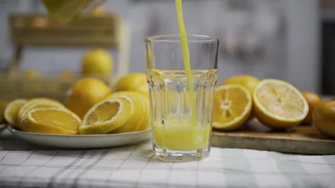Slow motion tracking shot of juice being poured into glass cup near orange Stock Footage 341273815