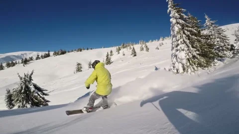 Slow motion tracking shot of a snowboarder on a bright sunny day cruising down Stock Footage