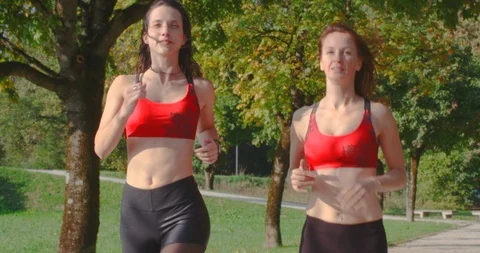 Slow motion tracking shot, two young pretty women running in park. Stock Footage 120235178