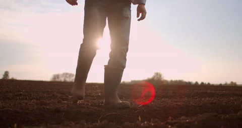 Slow motion tractor drivers boots walk across a plowed field at sunset after a Vídeo Stock 131918372