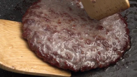 Slow motion of turning sizzling hamburger on dark gray fry pan close up. Stock Footage 99854861