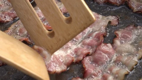 Slow motion of turning sliced bacon on dark gray fry pan close up. Stock-Footage 99851836