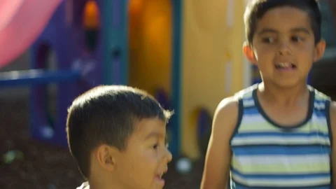 Slow motion of two boys jumping in front of swing set and facing the camera Stock Footage 92062799