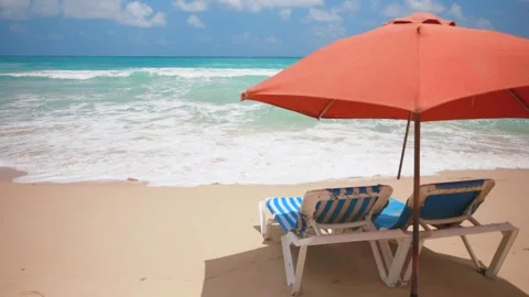 Slow motion of two empty blue sun loungers under the red parasol on the sandy Stock Footage 272612635
