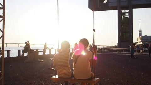 Slow motion. two kids looking on sunset while swinging in gold evening Stock Footage 128546019