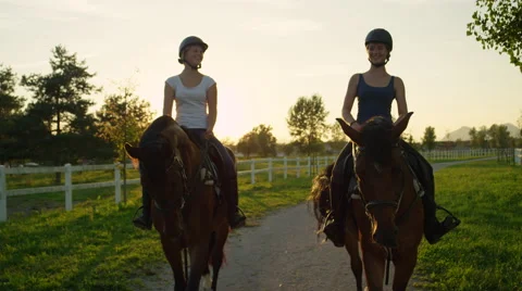 SLOW MOTION: Two laughing friends horseback riding brown horses at golden sunset Stock Footage