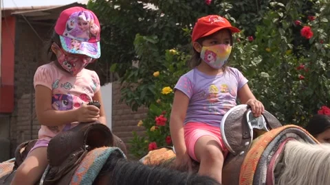 Slow motion of two little sisters riding horse wearing mask on family trip Stock-Footage 150924991