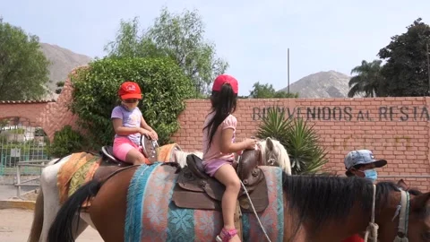 Slow motion of two little sisters riding horse wearing mask on family trip Stock Footage 150924992