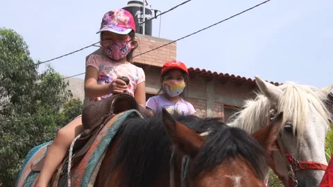 Slow motion of two little sisters riding horse wearing mask on family trip Stock Footage 150925593