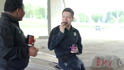 Slow motion two policemen drinking coffee and eating donut with appetite talk Stock Footage 112956764