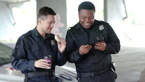 Slow motion two policemen drinking coffee and eating donut use phone talk near Stock Footage 112958206