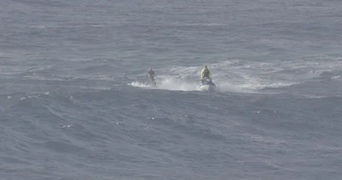 Slow motion of two pro surfers surfing across ocean on jet ski and surfing board Stock Footage 160105509