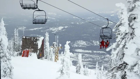 Slow motion of two skiers in red overalls carried by chairlift up to mountains Stock Footage 129116621