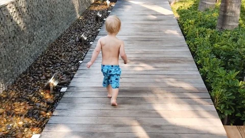 Slow motion.  two-year-old blond boy runs away on a wooden path . Stock Footage 104849136