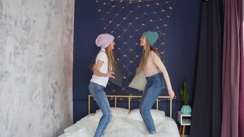Slow motion two young pretty girls jump on the bed and fight with pillows Stock Footage 104131486