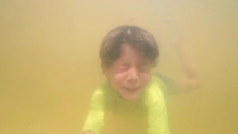 Slow motion underwater view of young boy diving into a murky thermal pool Vídeos de archivo 347660348