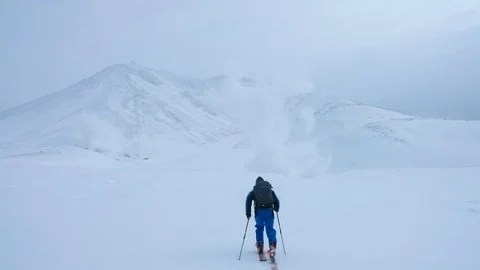 SLOW MOTION: Unrecognizable man hiking up a snowy mountain and towards a volcano Stock Footage 99449218