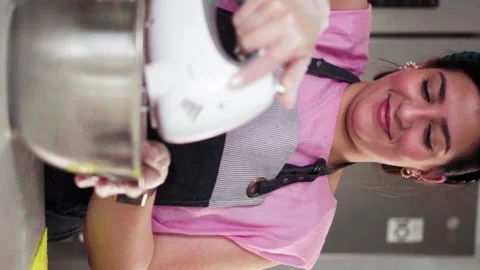 Slow motion vertical video of a smiling young woman whipping up cake mix Stock Footage 156878096