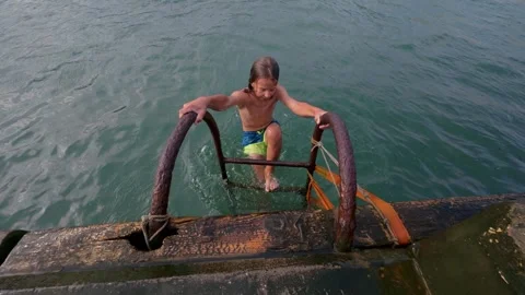 Slow motion video of an 11-year-old boy climbing a rusty ladder from the sea Stock Footage 317611640