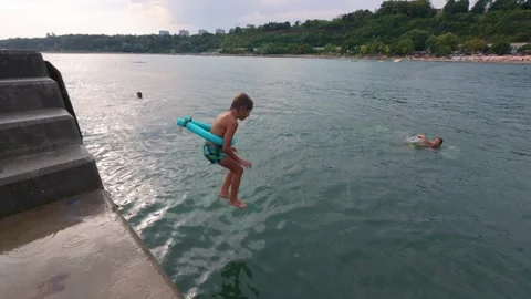 Slow motion video of an 8-year-old boy jumping into the sea with a pool noodle Stock-Footage 317611332