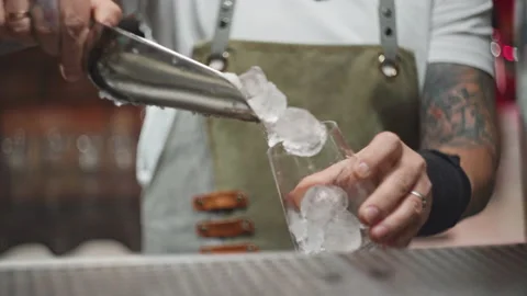 A slow-motion video of a bartender pouring ice into a glass at the bar. Stock Footage 228886972