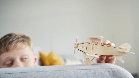 Slow motion video of boy playing with wooden plane on sofa Video stock 102591704