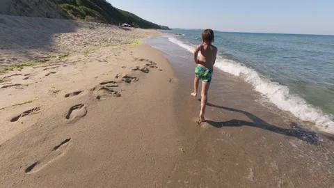 Slow motion video of a boy running through shallow waves on a sunny beach, water Stock Footage 313810443