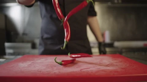 Slow motion video of a chef throwing red chili peppers on a cutting board. Stock Footage 237912859