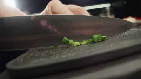 Slow-motion video close-up of cutting green onions with a knife on cutting board 库存影片 223412040