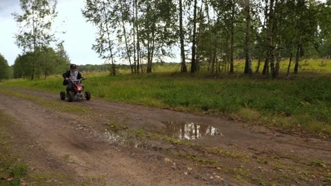 Slow motion video. In the forest, a child enjoys riding an ATV through puddles Stock Footage 253060241