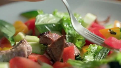 In the slow-motion video, a fork gently stirs a fresh green salad. Video stock 234021429