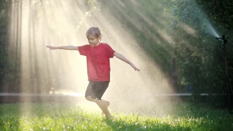 Slow motion video of funny boy playing with garden sprinkler in sunny backyard Stock Footage 252096320