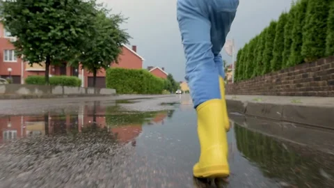 Slow motion video of little boy wearing yellow rubber boots running in puddle Stock Footage 157325543