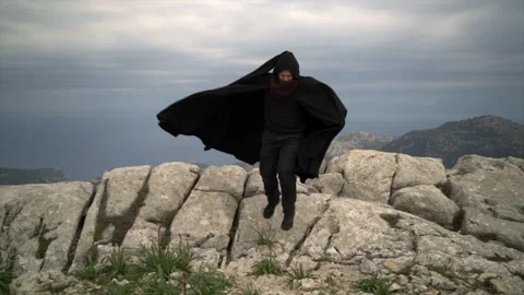Slow motion video of man with cape jumping from rocks. 스톡 동영상 153314012