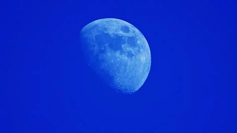 Slow-motion video of the moon glowing softly against a vibrant blue sky in Stock Footage 291886144