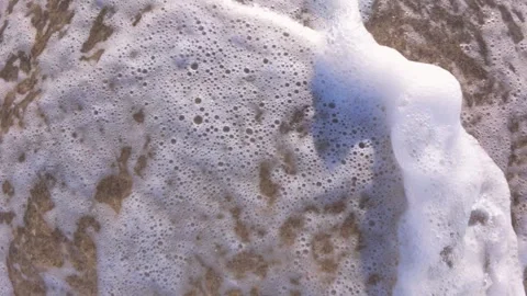 Slow motion video of ocean foam gently washing over wet sand on the beach Stock Footage 313844532