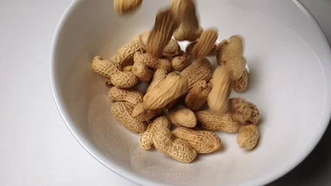 Slow-motion video of peanuts dropping into a white ceramic bowl. Video stock 160929252