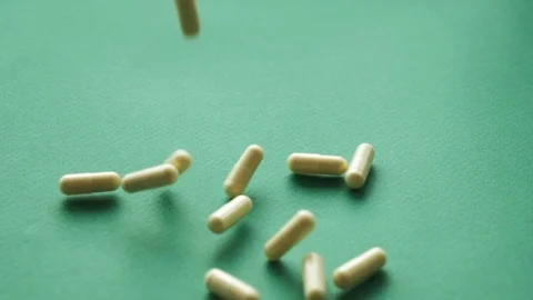 Slow motion video pills falling on green background. pills supplements closeup Stock Footage 125930352