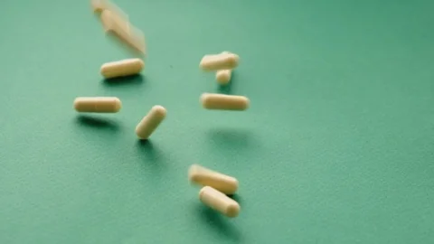 Slow motion video pills falling on green background. pills supplements closeup Stock-Footage 125930378