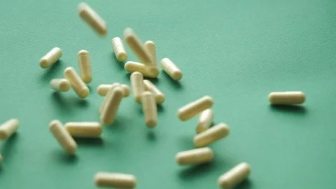 Slow motion video pills falling on green background. pills supplements closeup Stock-Footage 125930385