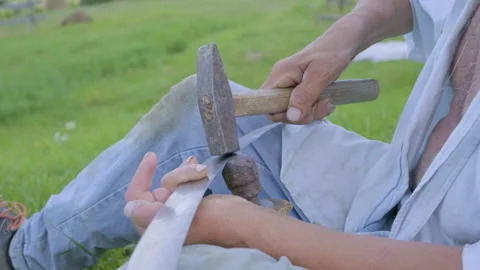 Slow motion video of senior man peening scythe blade with hammer. Stock Footage 136671014