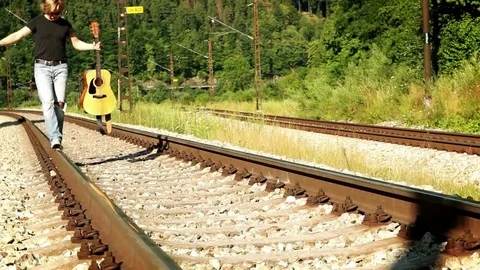 Slow-motion video of a teenager walking by the railway holding a guitar Stock Footage