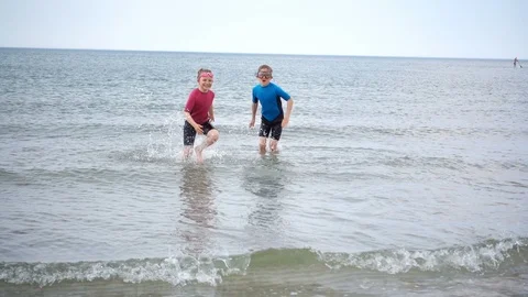 Slow-motion video of two happy children in neoprene swimsuits running on the  Stock Footage 111659899