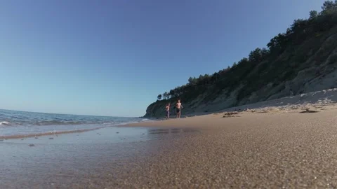 Slow motion video of two happy shirtless boys running barefoot along a sandy Stock Footage 313843171