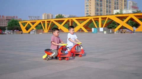 Slow motion video of two little Chinese boys playing with scooters on a square i Stock Footage 221458353