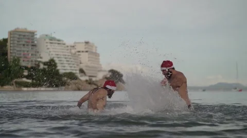 Slow motion video of two men with Santa Claus hats fighting in the beach spla Video stock 140940807