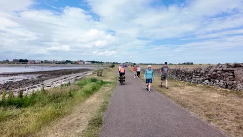 Slow motion view of cyclists and walkers moving along a seaside path beside dry Stock Footage 341395879